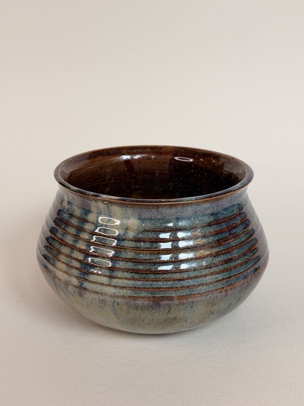 A rounded ceramic bowl with blue-green glaze, dark horizontal ridges and a warm brown interior