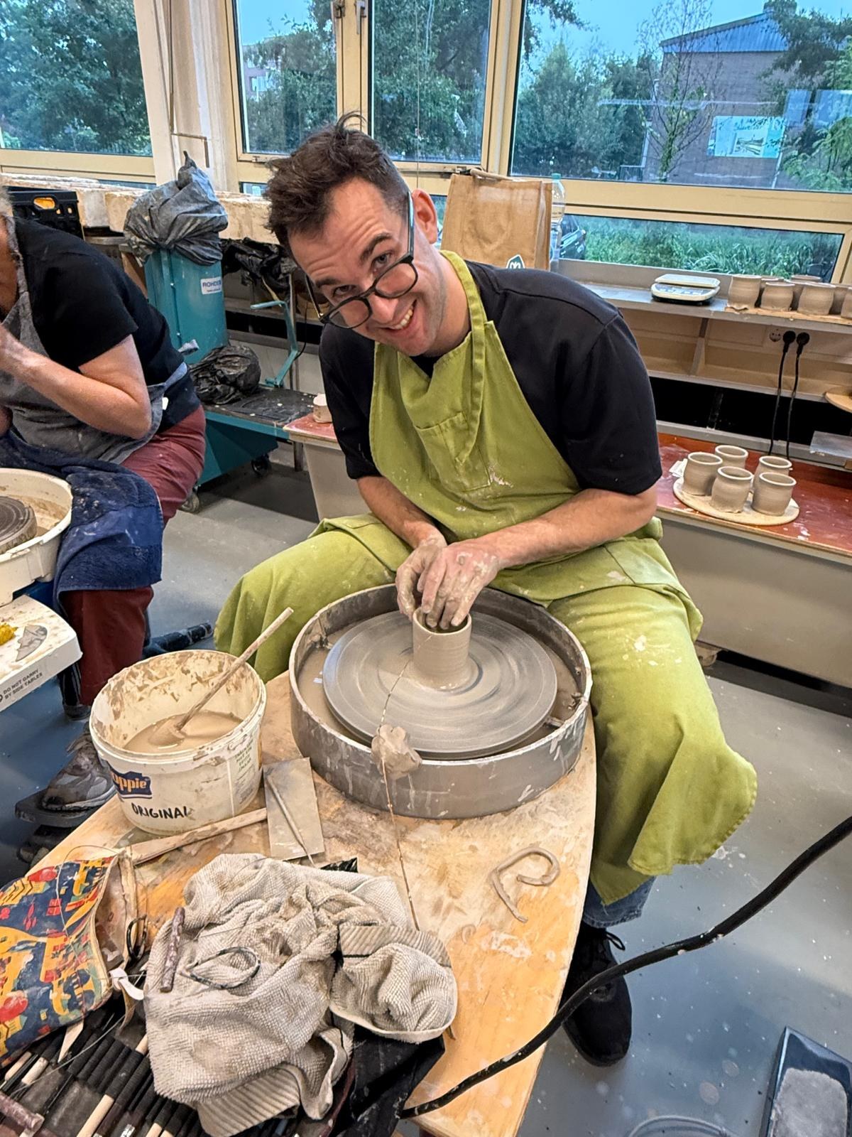 Michael smiling while throwing a pot at the wheel