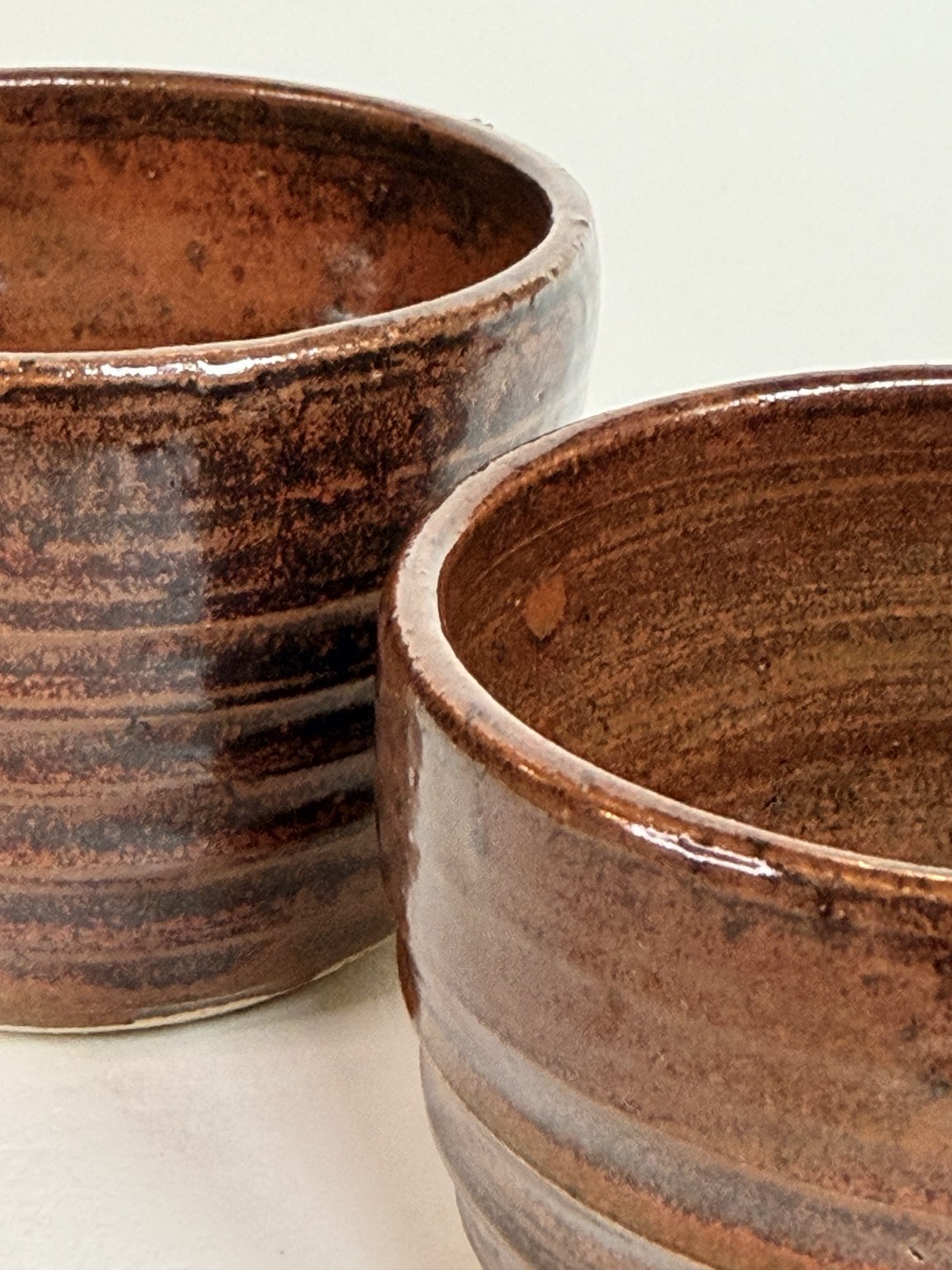 Close view of red glaze and turning lines across two ceramic forms